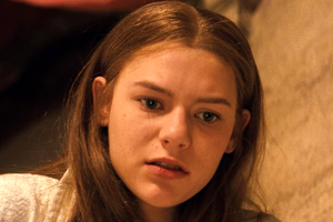 Młoda kobieta z długimi, prostymi włosami, z zamyśloną miną, patrzy w dół.