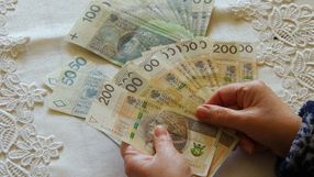 Dwie ręce trzymają banknoty w złotych: 50, 100, 200. Tło z koronką.