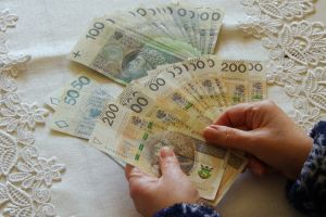 Dwie ręce trzymają banknoty w złotych: 50, 100, 200. Tło z koronką.