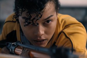 Młoda osoba w żółtej bluzie, skupiona, trzyma karabin, przygotowując się do strzału.