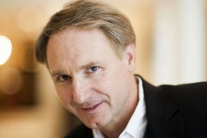 Mężczyzna z krótkimi włosami, lekko uśmiechnięty, w czarnej marynarce.