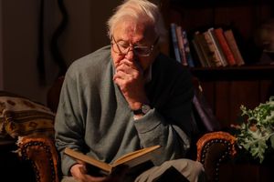 Na zdjęciu starszy mężczyzna w okularach, głęboko zamyślony, trzyma książkę w ciemnym wnętrzu.