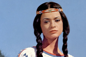 Młoda kobieta w tradycyjnym stroju, z warkoczami i barwną opaską na głowie, na tle nieba.