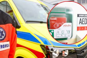 Na zdjęciu widać ratownika medycznego obok karetki oraz defibrylatora AED.