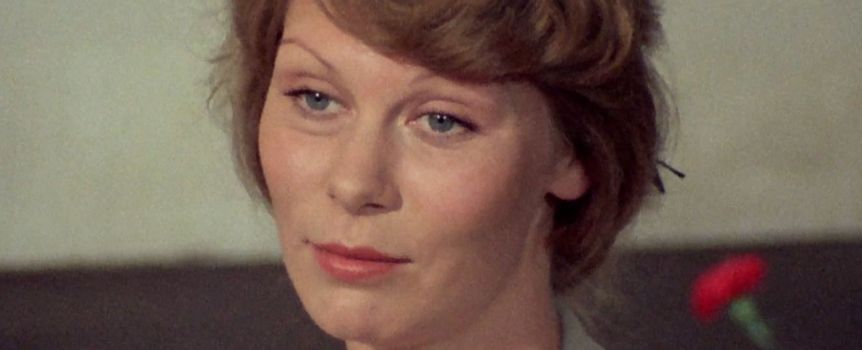 Na zdjęciu kobieta z krótkimi jasnobrązowymi włosami, w jasnej bluzce, z delikatnym uśmiechem.