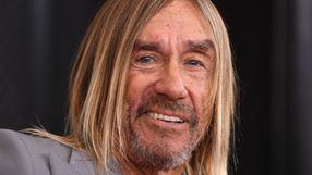 Mężczyzna z długimi, blond włosami i brodą, uśmiechający się, w szarym garniturze.