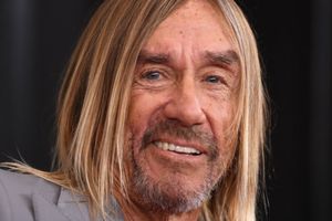Mężczyzna z długimi, blond włosami i brodą, uśmiechający się, w szarym garniturze.