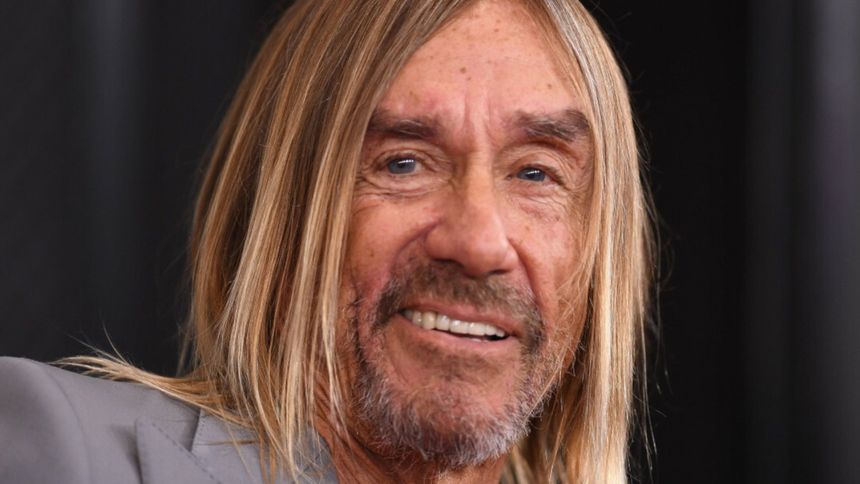 Mężczyzna z długimi, blond włosami i brodą, uśmiechający się, w szarym garniturze.