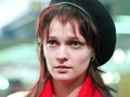 Młoda kobieta z długimi, brązowymi włosami, w beret i czerwoną chustą. Wyraz twarzy poważny.