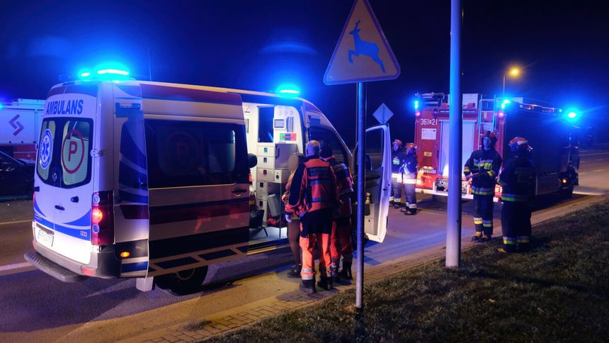 Na zdjęciu karetka i strażacy nocą, w tle niebieskie światła i znak drogowy.