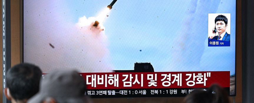 Na tle ekranu telewizyjnego wystrzał rakiety, widać ludzi obserwujących wydarzenie.