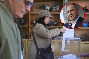 Kobieta głosuje w lokalu wyborczym, w tle mężczyzna i szafa z przedmiotami mechanicznymi.