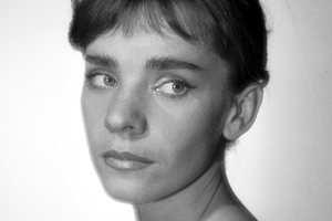 Portret młodej kobiety z krótkimi, ciemnymi włosami, patrzącej w bok na tle jasnej ściany.