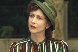 Kobieta z falującymi włosami, w zielonym kapeluszu oraz kolorowej bluzce, uważnie słucha.