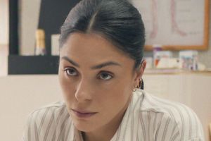 Kobieta z ciemnymi włosami, w koszuli w paski, skupiona na rozmowie. Tło biurowe.