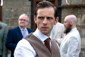 Mężczyzna w eleganckim kamizelce, z poważnym wyrazem twarzy, na tle innych gości.