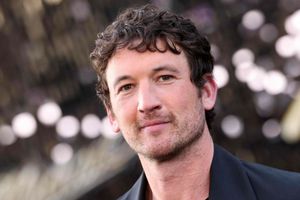 Mężczyzna z ciemnymi, kręconymi włosami, uśmiecha się na tle rozmytych świateł.