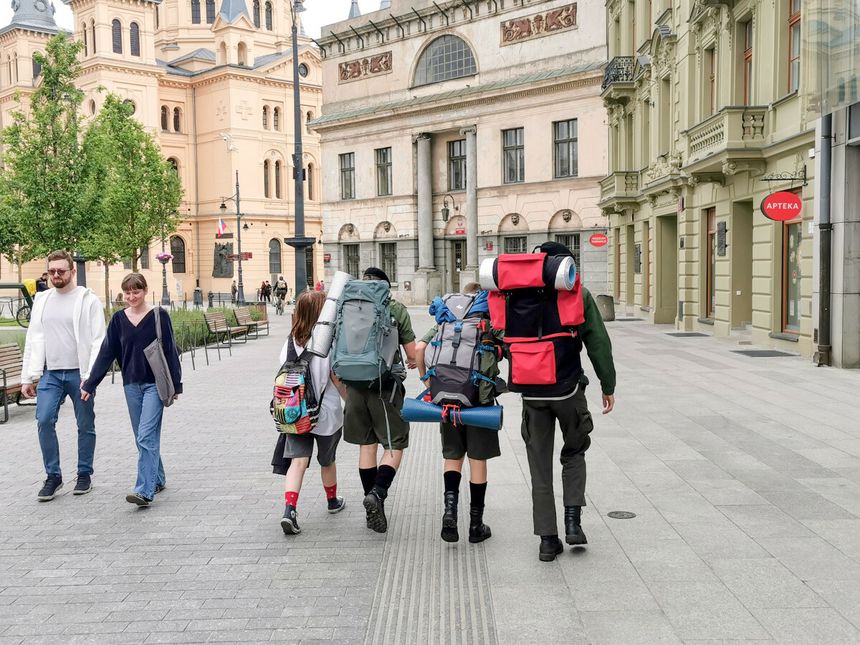 Na zdjęciu grupa osób z plecakami idzie ulicą, w tle widoczna architektura miasta.