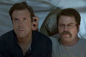 Dwaj mężczyźni siedzą w namiocie, jeden z nich słucha muzyki przez słuchawki, drugi skupiony.