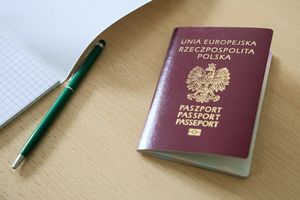 Na stole leży paszport Polski, zielony długopis i kartka w kratkę. Tło jasne.