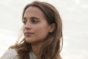 Kobieta z długimi, brązowymi włosami, patrzy w dal, na tle pochmurnego nieba.