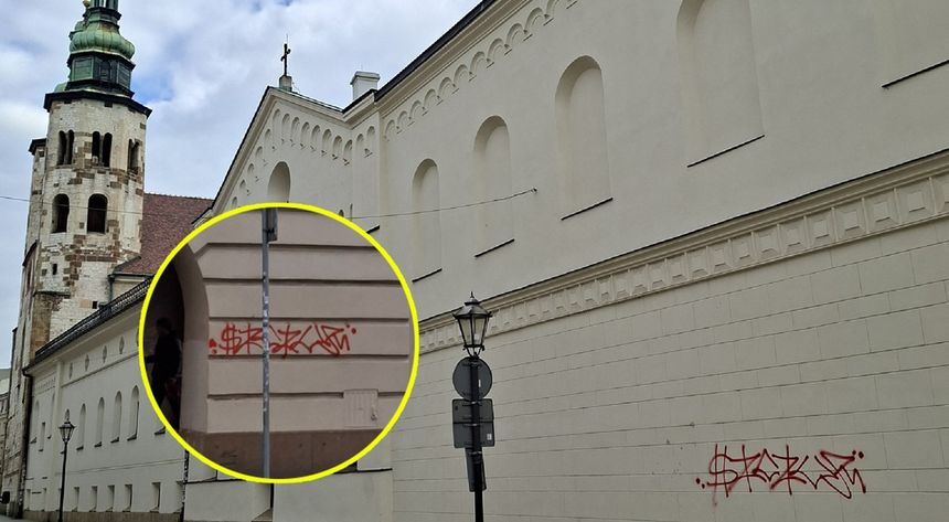 Widok ściany z graffiti w czerwonym kolorze obok budynku z wieżą i lampą uliczną.