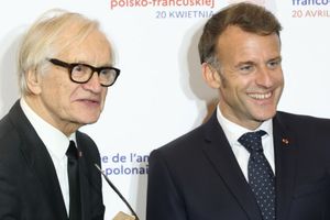 Na zdjęciu dwaj mężczyźni w garniturach, uśmiechają się do aparatu. Tło z logo wydarzenia.