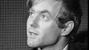 Na czarno-białym zdjęciu młody mężczyzna z jasnymi włosami, patrzy w górę, uśmiechając się.