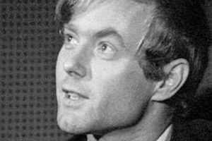 Na czarno-białym zdjęciu młody mężczyzna z jasnymi włosami, patrzy w górę, uśmiechając się.