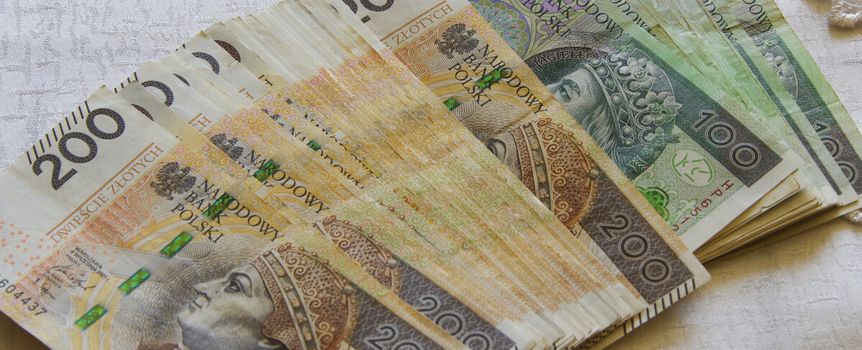 Stosik polskich banknotów o nominałach 100 i 200 zł leży na białym tle.