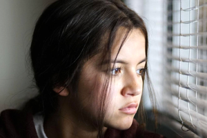 Młoda dziewczyna z długimi włosami, smutno patrzy przez okno.