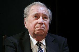 Starszy mężczyzna w garniturze, z poważnym wyrazem twarzy, na ciemnym tle.