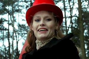 Na zdjęciu uśmiechająca się kobieta w czerwonym kapeluszu, w tle drzewa.