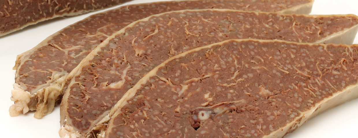 Plastry ciemnej, mięsnej wędliny na białym tle, o jednolitej fakturze i wyglądzie.