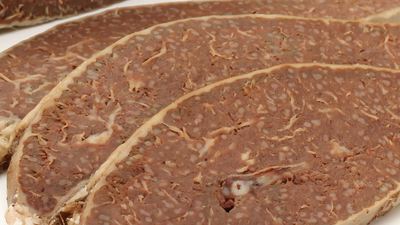 Plastry ciemnej, mięsnej wędliny na białym tle, o jednolitej fakturze i wyglądzie.