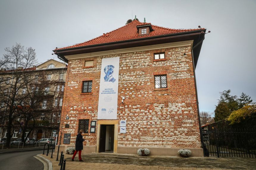 Muzeum Stanisława Wyspiańskiego, ceglana fasada, osoba wchodząca do budynku, szare niebo.
