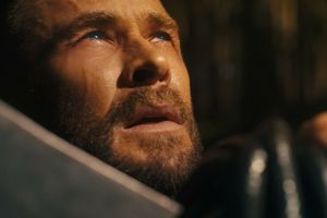 Mężczyzna z brodą patrzy w górę, w tle nieostre drzewo, wyraz twarzy napięty.