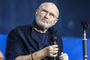 Na zdjęciu starszy mężczyzna z mikrofonem, w ciemnej bluzie, z siwą brodą i okularami.