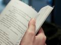 Zdjęcie przedstawia rękę trzymającą otwartą książkę z tekstem na stronach.