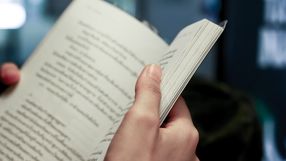 Zdjęcie przedstawia rękę trzymającą otwartą książkę z tekstem na stronach.