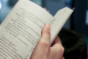 Zdjęcie przedstawia rękę trzymającą otwartą książkę z tekstem na stronach.