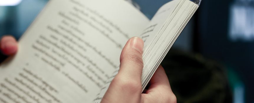 Zdjęcie przedstawia rękę trzymającą otwartą książkę z tekstem na stronach.