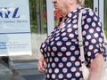 Na zdjęciu widać starszą kobietę w granatowej bluzce w białe i r&oacute;żowe kropki, stojącą przed budynkiem.