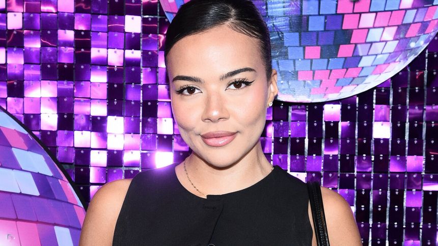 Lexy Chaplin w czarnej sukience przed błyszczącą, fioletową ścianą.