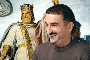 Mężczyzna w swetrze uśmiecha się, w tle postać króla w złotej koronie i szacie.