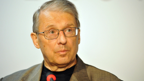 Mężczyzna w okularach, z siwymi włosami, w garniturze, patrzy poważnie w stronę kamery.