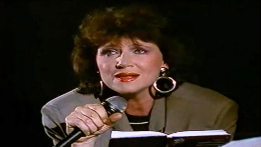 Na zdjęciu kobieta z mikrofonem, w dużych kolczykach, wyraża emocje podczas występu.