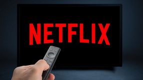 Zdalny pilot trzymany w ręku, na ekranie wyświetla logo Netflix w czerwonym kolorze.