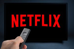 Zdalny pilot trzymany w ręku, na ekranie wyświetla logo Netflix w czerwonym kolorze.