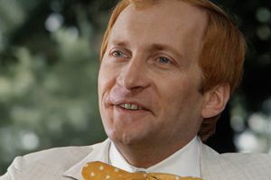 Na zdjęciu uśmiechający się mężczyzna w jasnym garniturze i żółtym krawacie.
